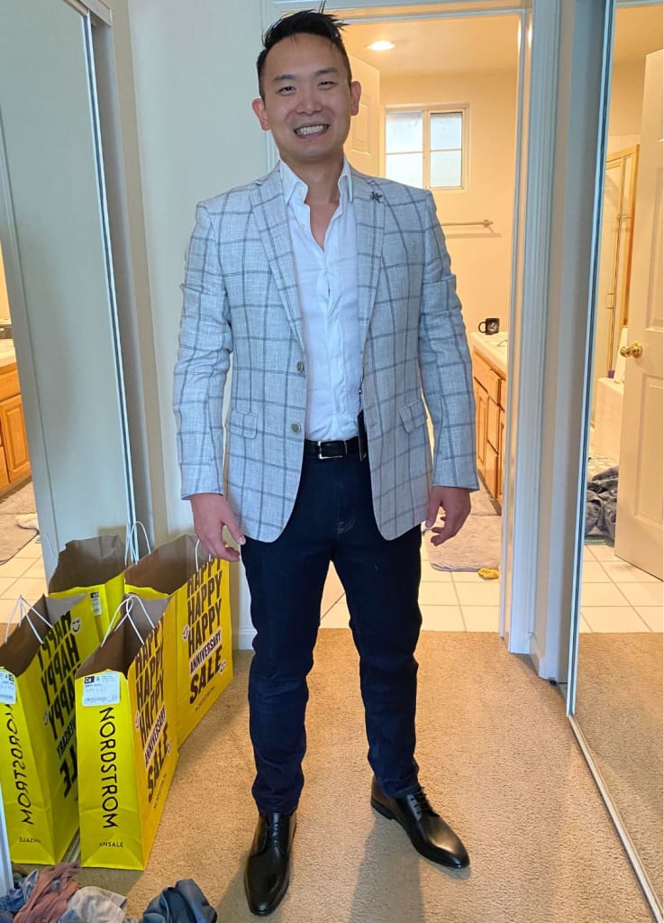 A person in a blazer and dark pants stands in a room with shopping bags labeled "Nordstrom" nearby.